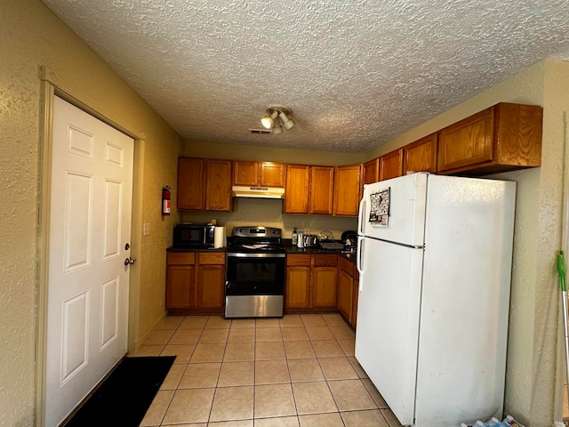 kitchen featuring light tile patterned flooring, a textured ceiling, white fridge, and stainless steel electric range