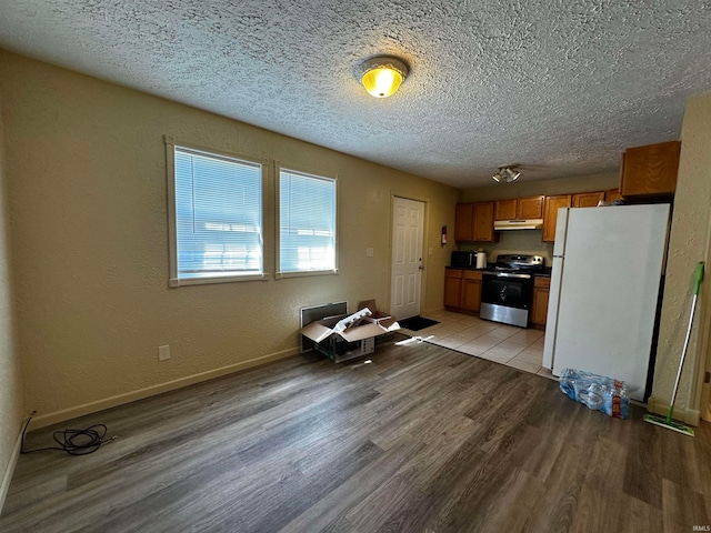 kitchen featuring stainless steel electric stove, light wood-type flooring, a textured ceiling, and white refrigerator