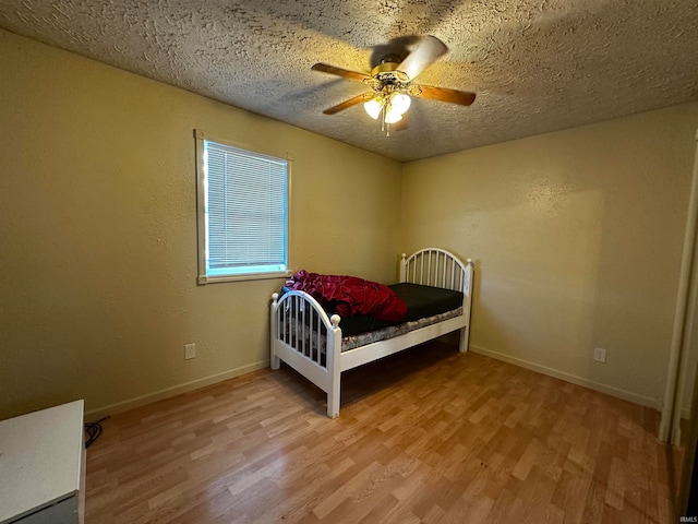 bedroom with ceiling fan, light wood-type flooring, and a textured ceiling