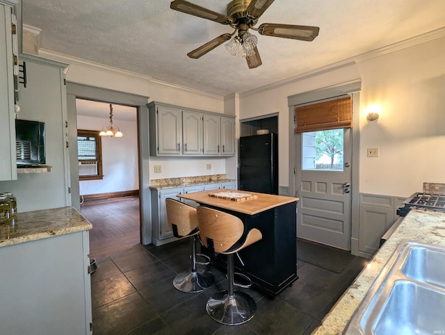 kitchen with a textured ceiling, dark hardwood / wood-style floors, ceiling fan with notable chandelier, ornamental molding, and black refrigerator