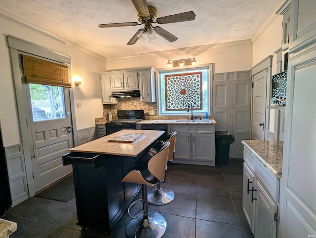 kitchen with dark tile patterned flooring, tasteful backsplash, crown molding, a center island, and black gas stove