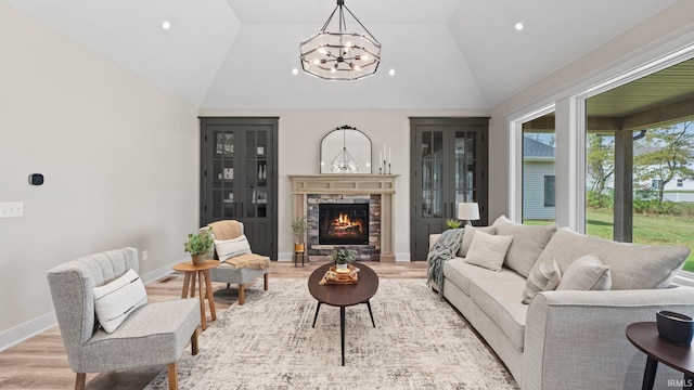 living room featuring a notable chandelier, light wood-type flooring, lofted ceiling, and a stone fireplace