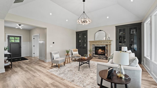 living room featuring a stone fireplace, light wood-type flooring, and vaulted ceiling