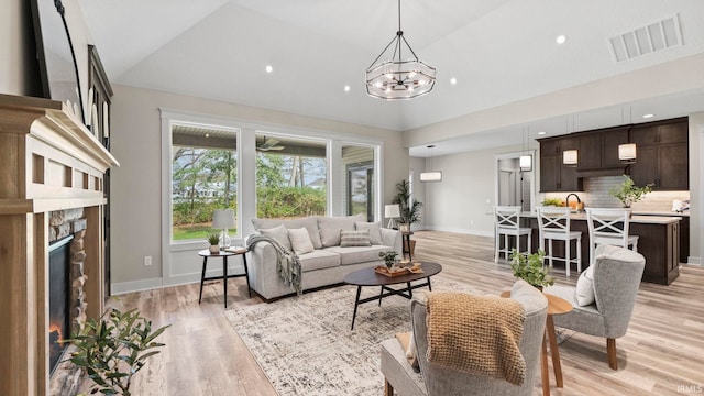 living room featuring a stone fireplace, vaulted ceiling, a chandelier, and light hardwood / wood-style flooring