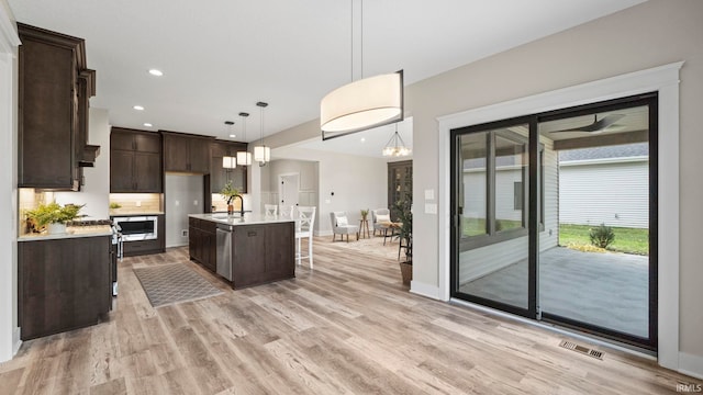 kitchen featuring hanging light fixtures, sink, dark brown cabinets, a kitchen island with sink, and light hardwood / wood-style floors