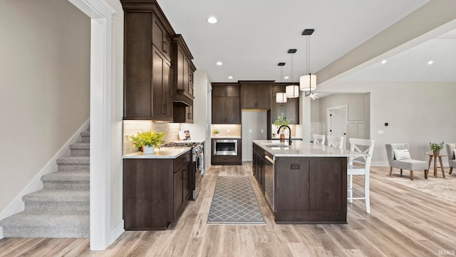 kitchen featuring stainless steel appliances, hanging light fixtures, sink, and light hardwood / wood-style flooring