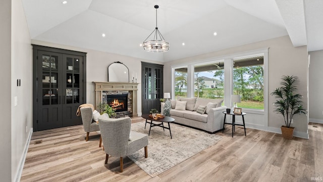 living room with an inviting chandelier, vaulted ceiling, light hardwood / wood-style floors, and a stone fireplace