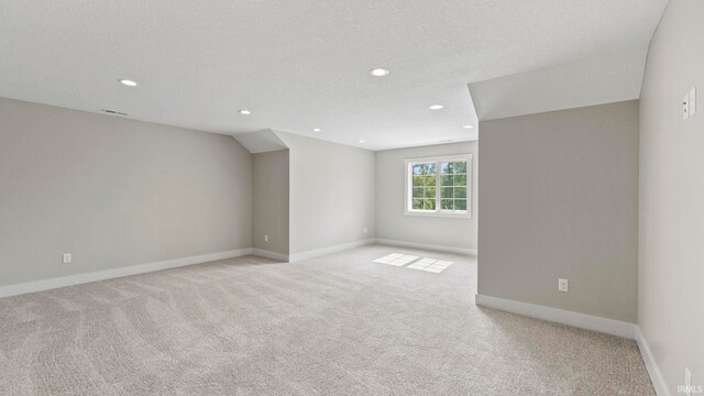 unfurnished room featuring lofted ceiling, a textured ceiling, and light colored carpet