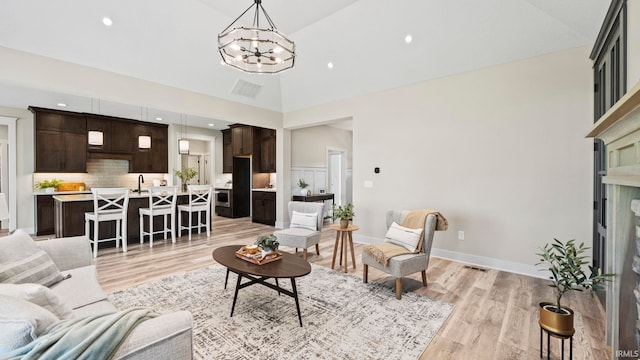 living room with sink, light wood-type flooring, a chandelier, and high vaulted ceiling