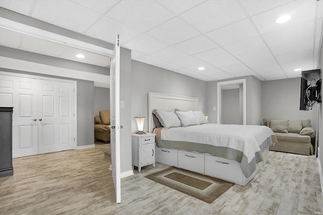 bedroom with a drop ceiling, light wood-type flooring, and a closet