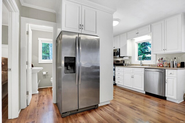 kitchen with appliances with stainless steel finishes, crown molding, light hardwood / wood-style floors, and white cabinetry