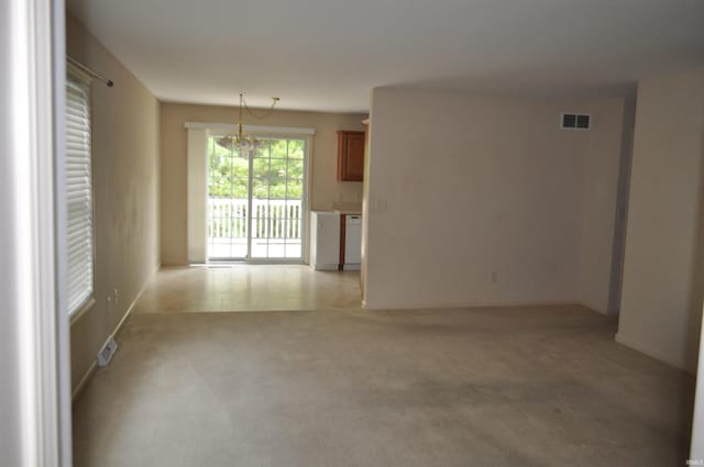 carpeted empty room with an inviting chandelier