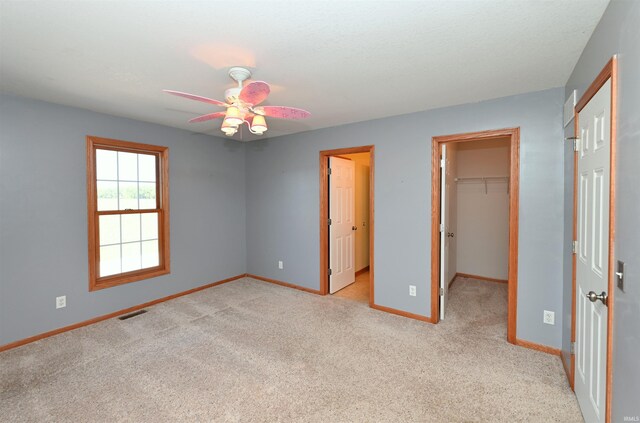 unfurnished bedroom with ceiling fan, a closet, light carpet, and a walk in closet