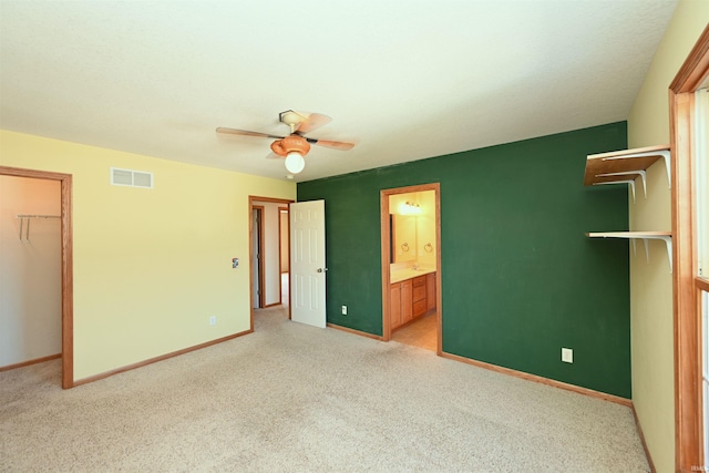 unfurnished bedroom with a closet, ceiling fan, ensuite bathroom, a walk in closet, and light carpet