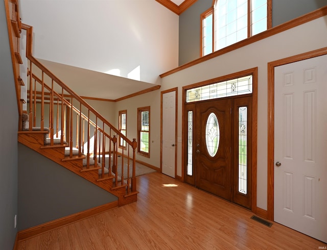 foyer with light wood-type flooring, crown molding, a towering ceiling, and a wealth of natural light