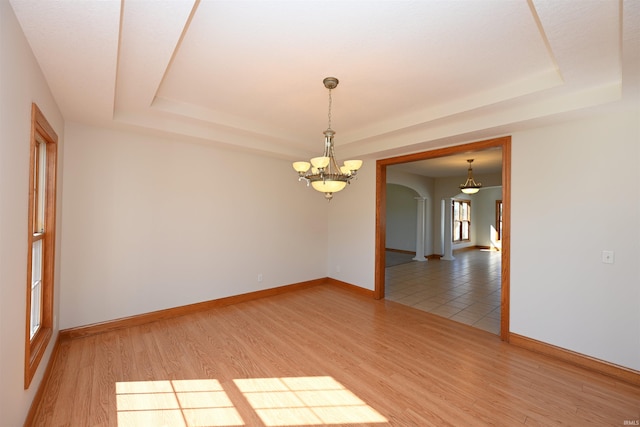 empty room with an inviting chandelier, a tray ceiling, and hardwood / wood-style flooring