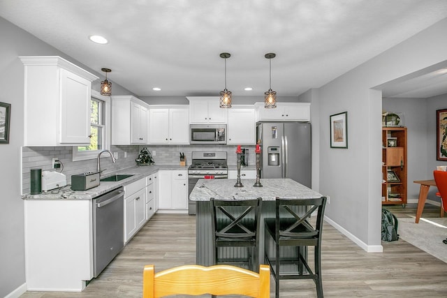 kitchen featuring appliances with stainless steel finishes, a kitchen island, light hardwood / wood-style flooring, decorative light fixtures, and sink