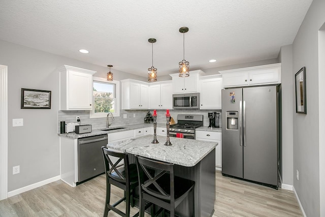 kitchen featuring appliances with stainless steel finishes, white cabinetry, a kitchen island, pendant lighting, and sink