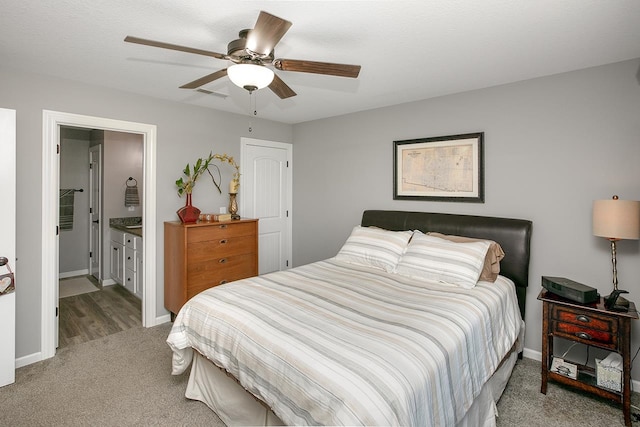 bedroom with ceiling fan, light colored carpet, and ensuite bath