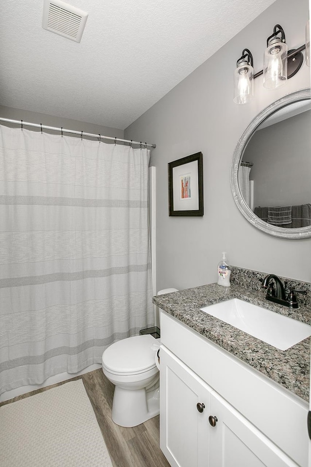 bathroom with a textured ceiling, a shower with shower curtain, hardwood / wood-style floors, vanity, and toilet