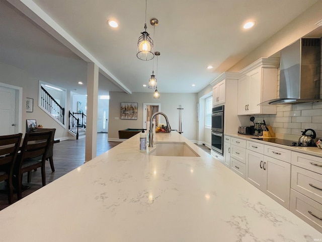 kitchen with sink, tasteful backsplash, wall chimney exhaust hood, white cabinetry, and double oven