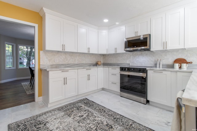 kitchen with appliances with stainless steel finishes, tasteful backsplash, light wood-type flooring, and white cabinets