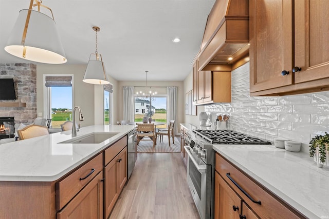 kitchen featuring a stone fireplace, sink, pendant lighting, appliances with stainless steel finishes, and a center island with sink