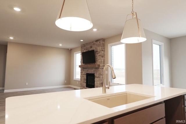 kitchen with wood-type flooring, a stone fireplace, hanging light fixtures, and sink