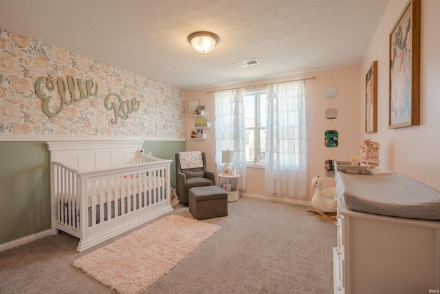 carpeted bedroom with a textured ceiling and a nursery area