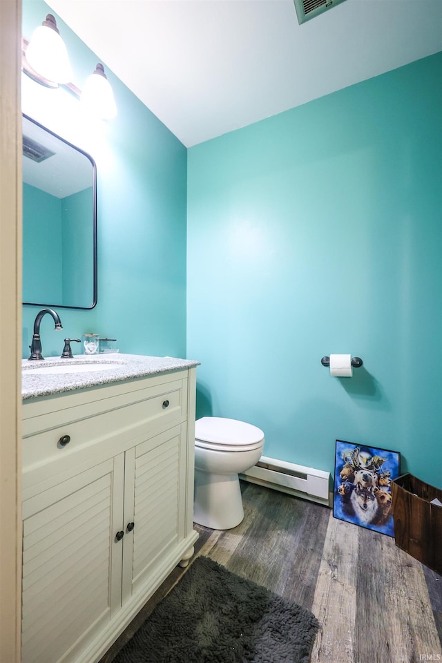 bathroom featuring hardwood / wood-style floors, baseboard heating, vanity, and toilet