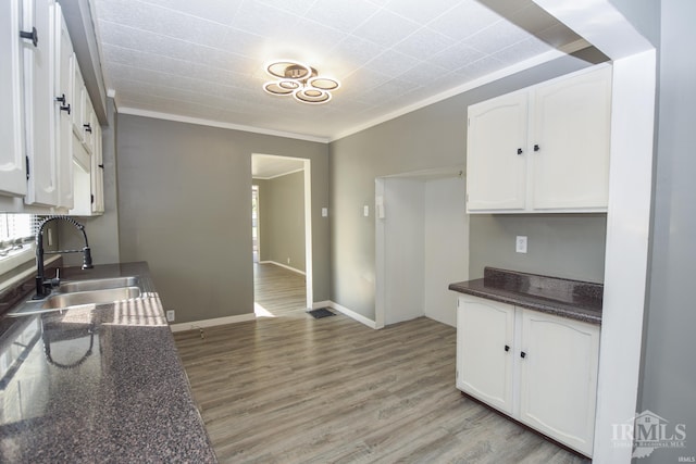 kitchen with light hardwood / wood-style flooring, white cabinetry, ornamental molding, and sink