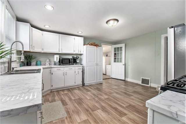 kitchen featuring light stone counters, sink, white cabinetry, separate washer and dryer, and light hardwood / wood-style floors