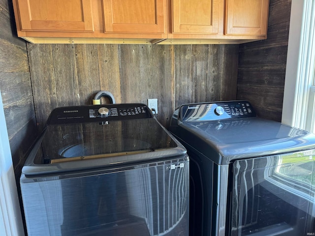 laundry room featuring cabinets, wooden walls, and washer and clothes dryer