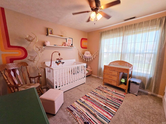 bedroom with carpet floors, a nursery area, a textured ceiling, and ceiling fan