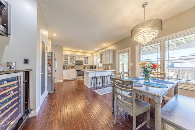 dining space with a textured ceiling, an inviting chandelier, beverage cooler, and dark wood-type flooring