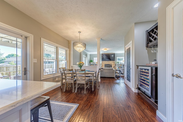 dining room featuring a textured ceiling, dark wood-type flooring, beverage cooler, a fireplace, and indoor bar