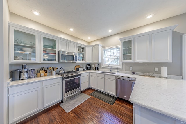 kitchen featuring appliances with stainless steel finishes, white cabinetry, light stone counters, dark hardwood / wood-style flooring, and sink