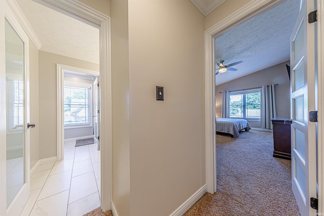 hallway with a textured ceiling, ornamental molding, vaulted ceiling, and light carpet