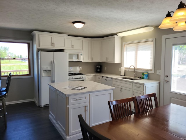 kitchen with a center island, sink, white cabinets, hanging light fixtures, and white appliances