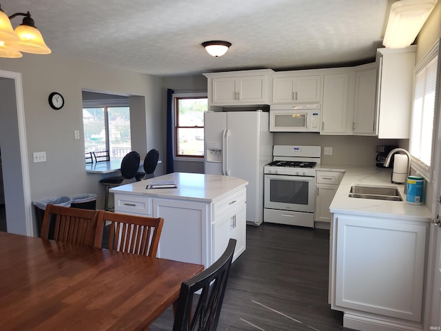 kitchen with sink, white appliances, a kitchen island, decorative light fixtures, and dark hardwood / wood-style floors