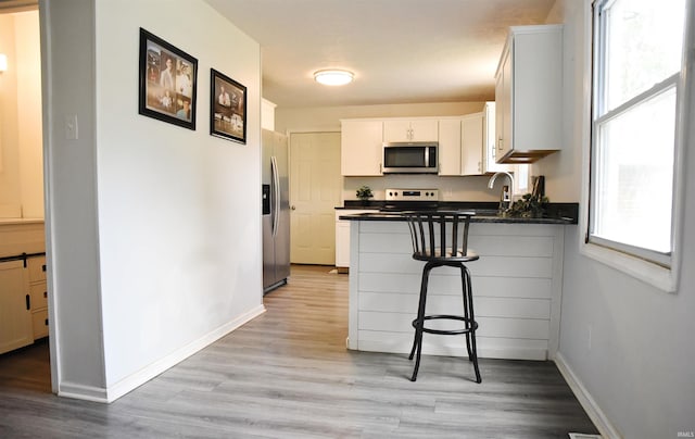 kitchen featuring light hardwood / wood-style floors, a breakfast bar, white cabinets, kitchen peninsula, and stainless steel appliances