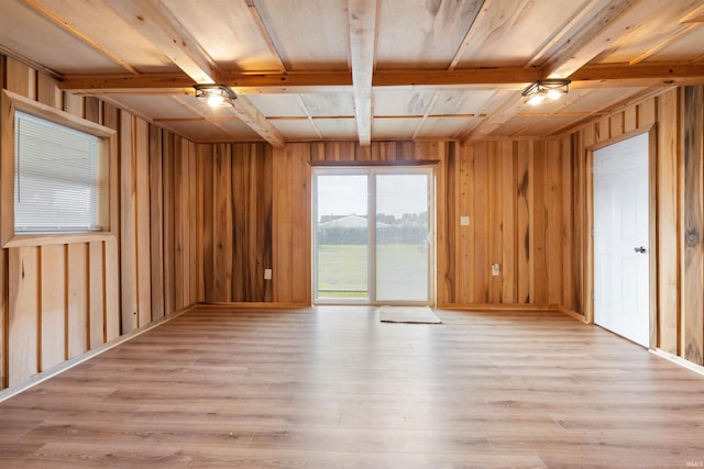 unfurnished room with beamed ceiling, wood walls, and light hardwood / wood-style floors