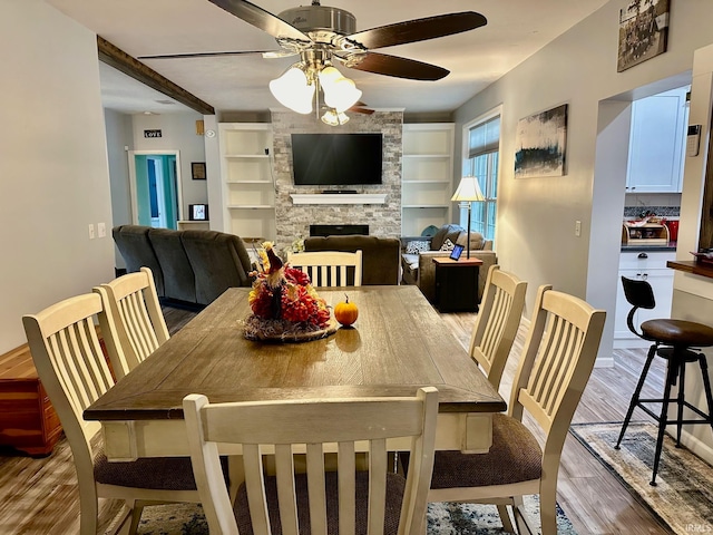 dining space featuring wood-type flooring, a fireplace, ceiling fan, and built in shelves