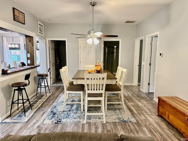 dining space with ceiling fan with notable chandelier and hardwood / wood-style flooring