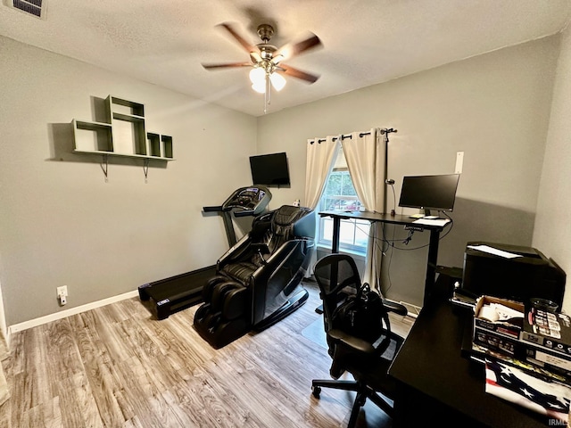 workout room with light wood-type flooring, a textured ceiling, and ceiling fan