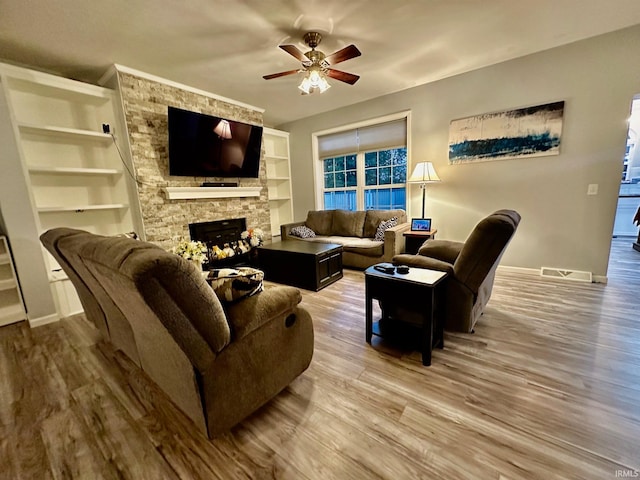 living room featuring wood-type flooring, ceiling fan, built in shelves, and a fireplace