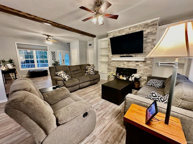 living room with ceiling fan, a stone fireplace, beamed ceiling, and light hardwood / wood-style flooring