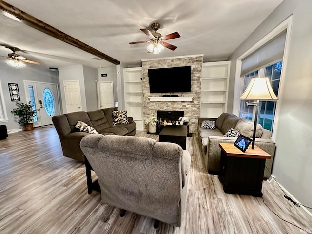 living room featuring ceiling fan, light wood-type flooring, a fireplace, and built in features