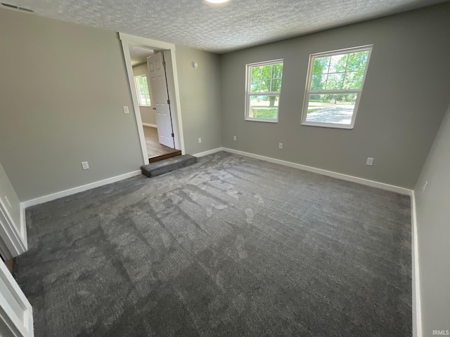 spare room featuring a textured ceiling and dark colored carpet