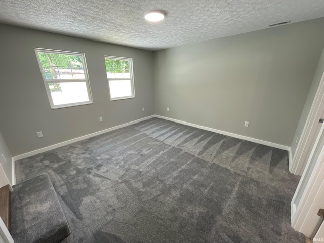 unfurnished room featuring a textured ceiling and dark colored carpet